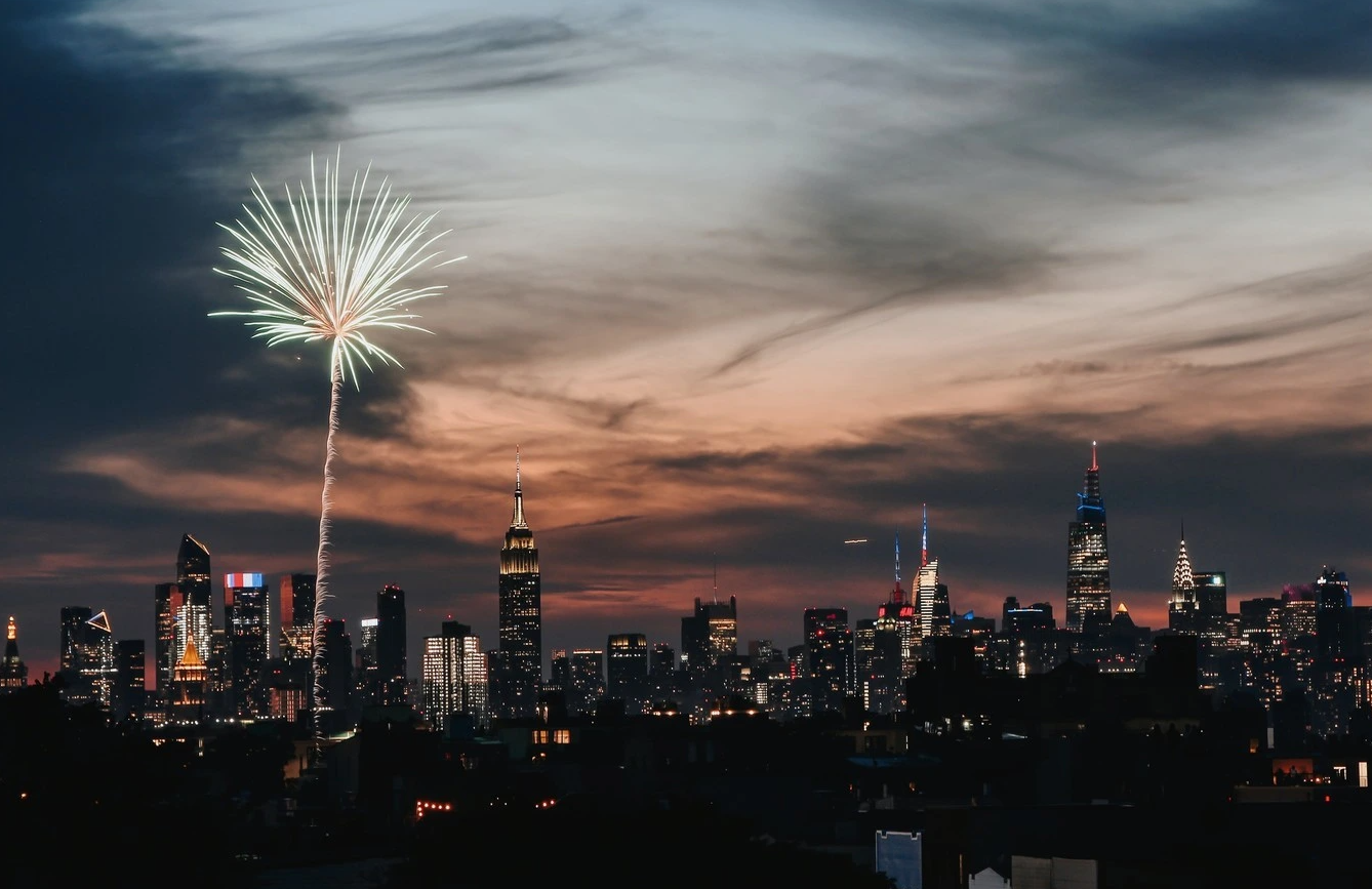 A city skyline at dusk with fireworks exploding in the sky.