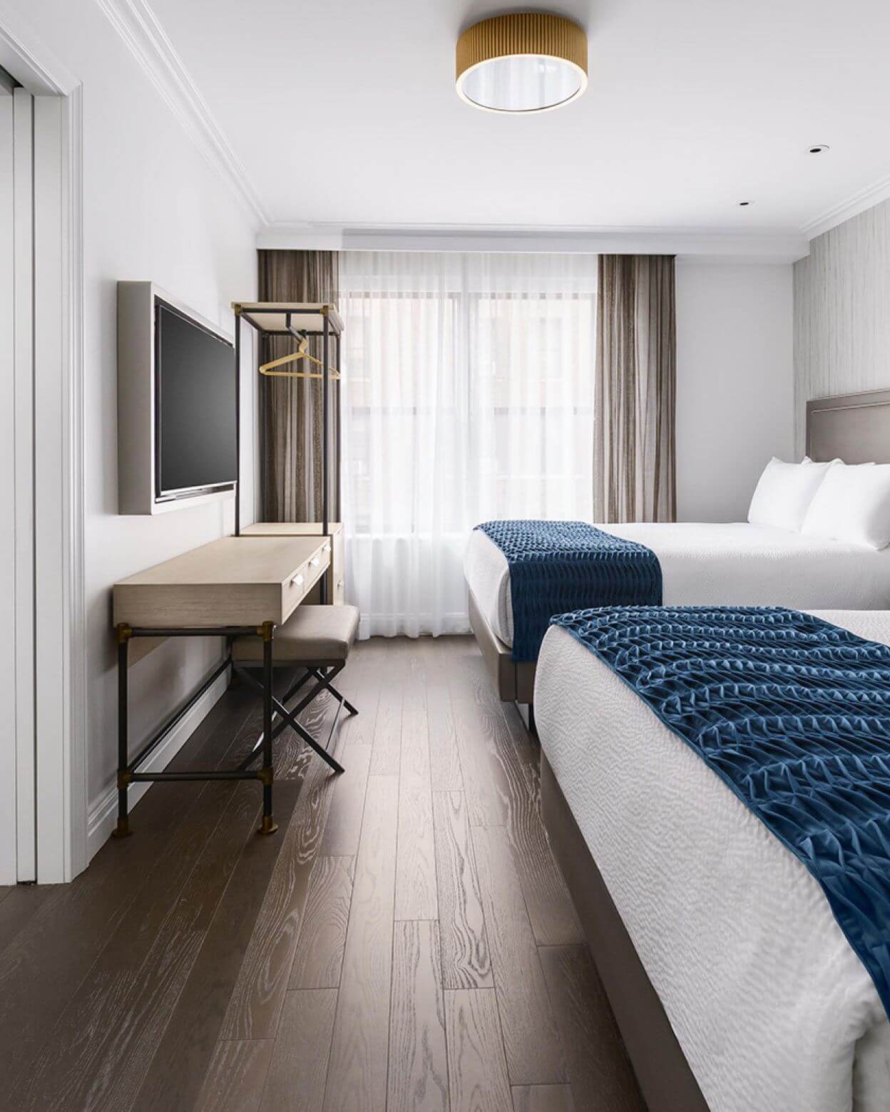 A hotel room with two beds, a desk, and a TV.