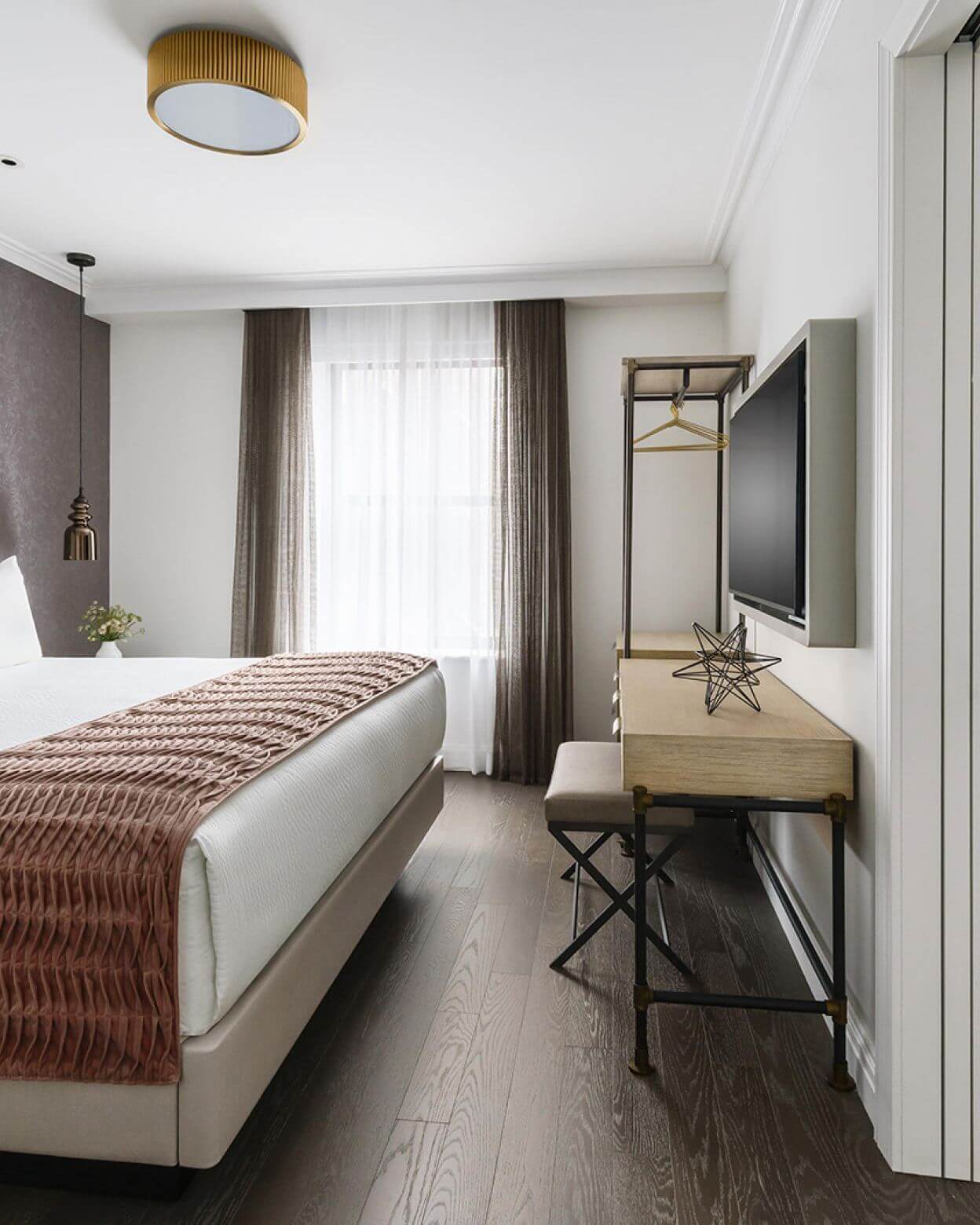A hotel room with a bed, desk, TV, and window