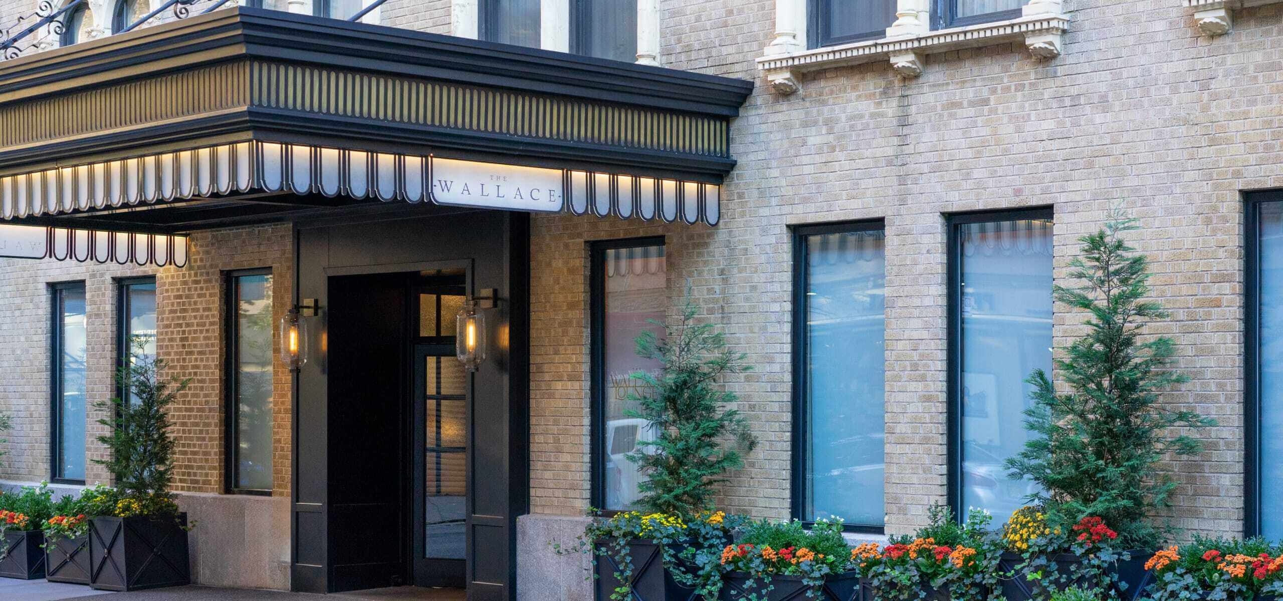 The entrance of a brick building with a striped awning and planters