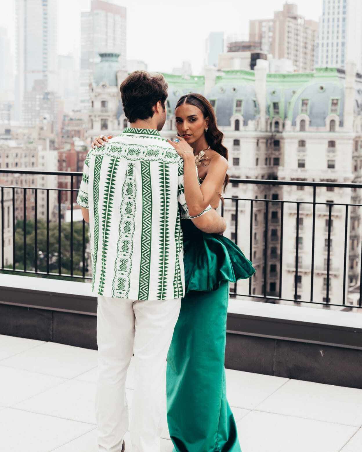 A couple stands on a rooftop with a city view