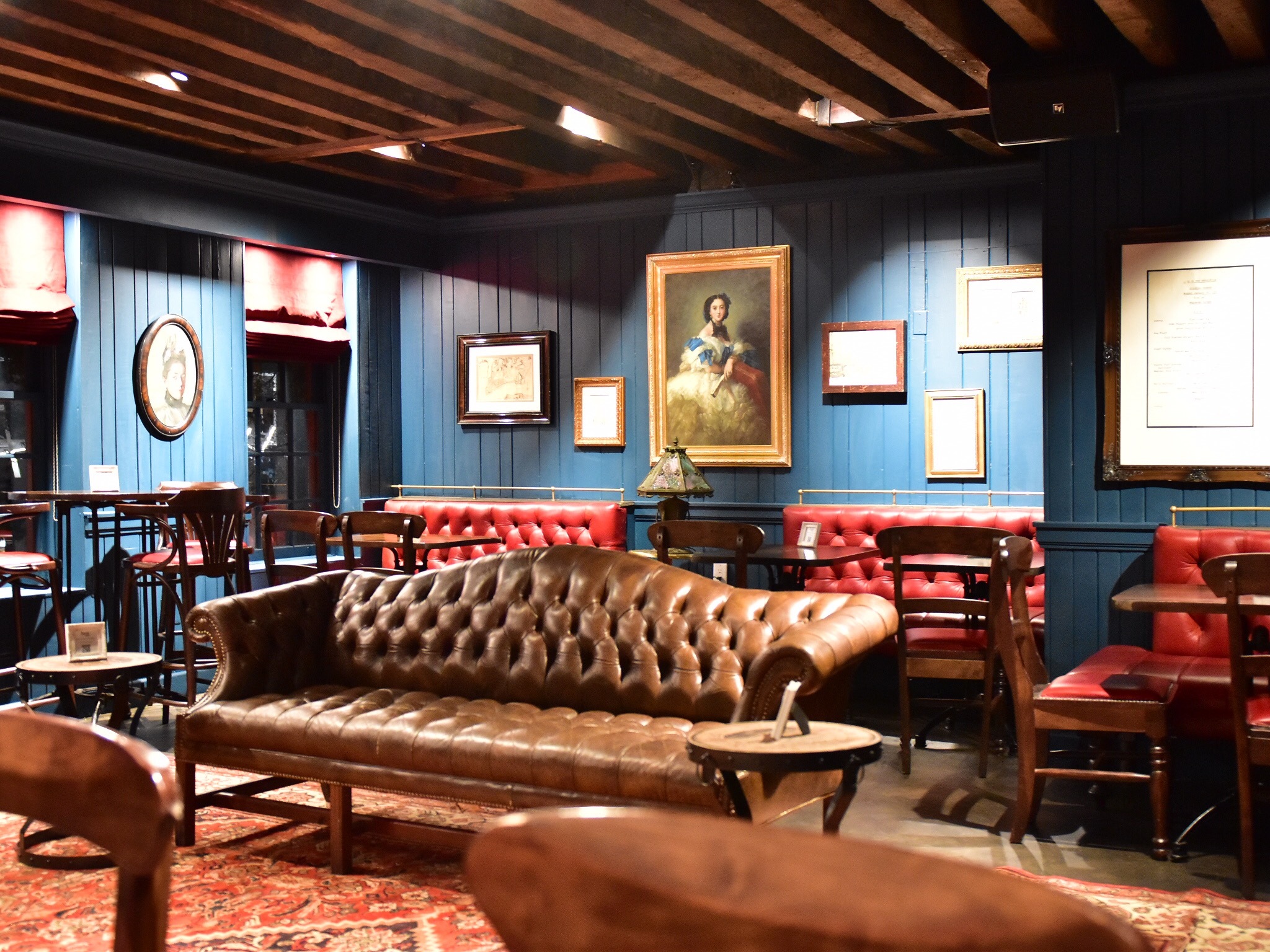 A cozy lounge area with a brown leather sofa, wooden chairs, and blue walls adorned with framed artwork.