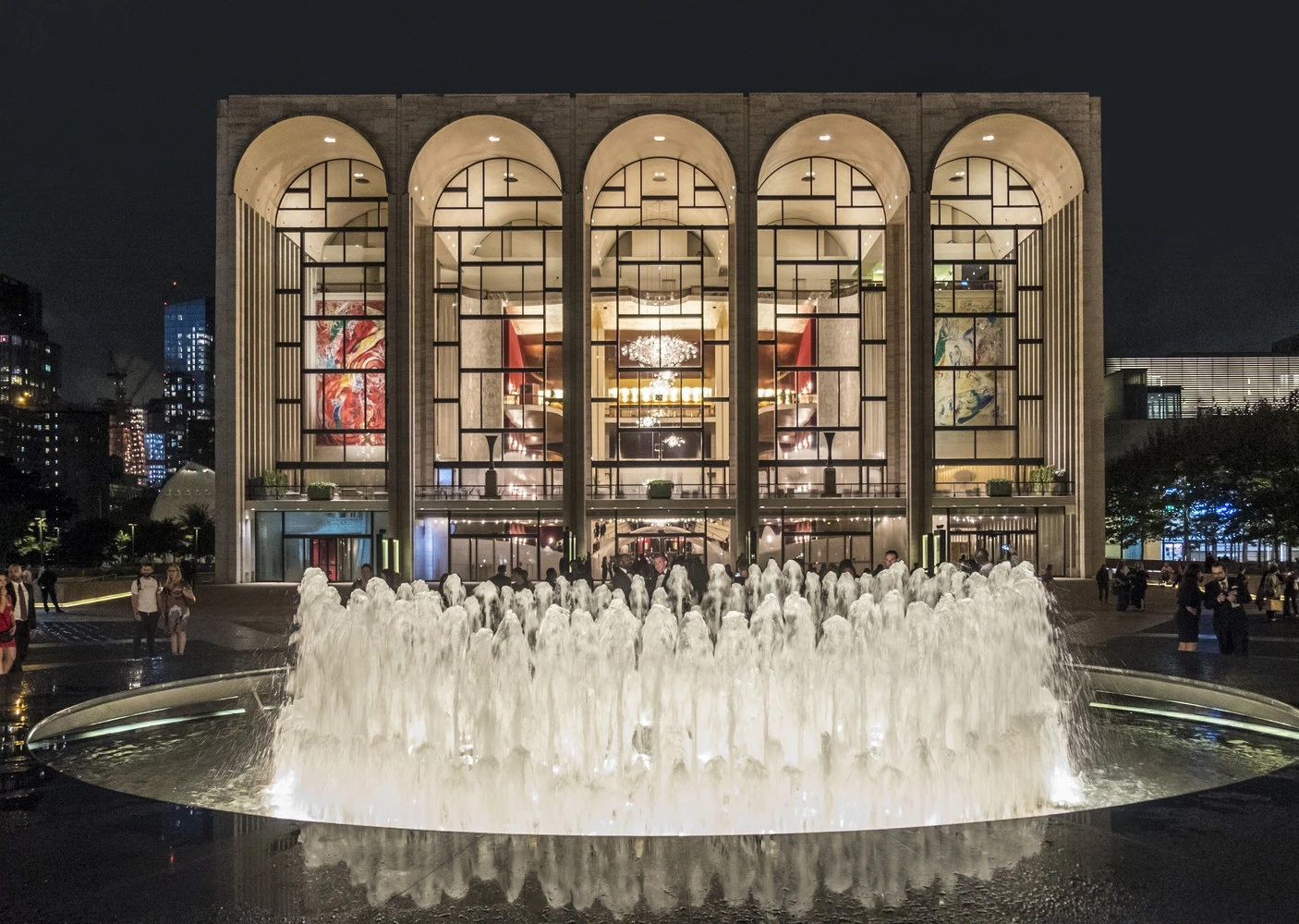 A large building with arched windows and a fountain in front of it at night.