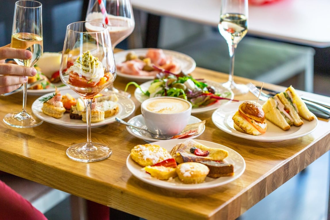 Breakfast Buffet Concept, Man's Hand with Glass of Champagne - Image by Ksenija Toyechkina / Shutterstock.com