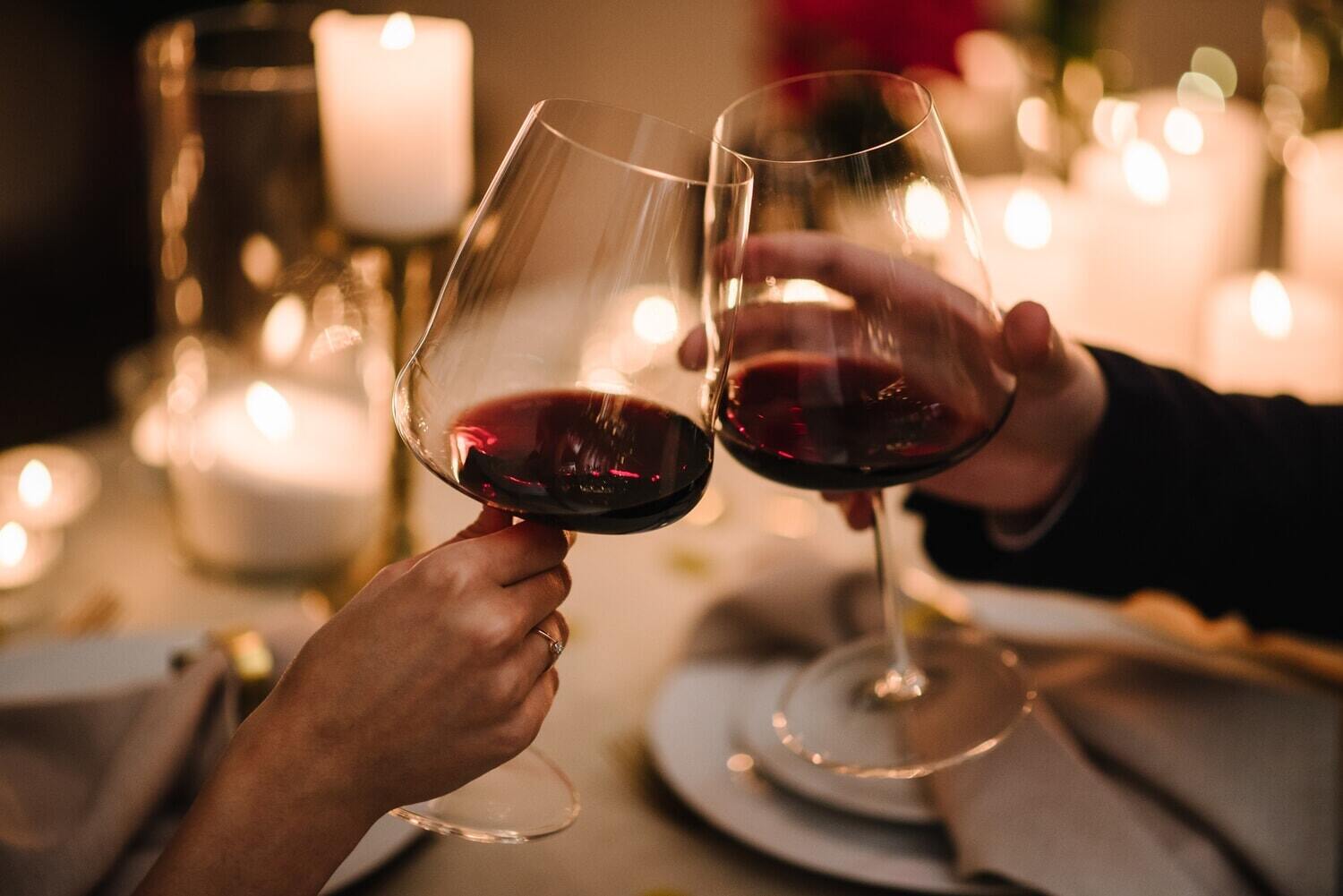 Two people clinking wine glasses at a romantic dinner table with candles.