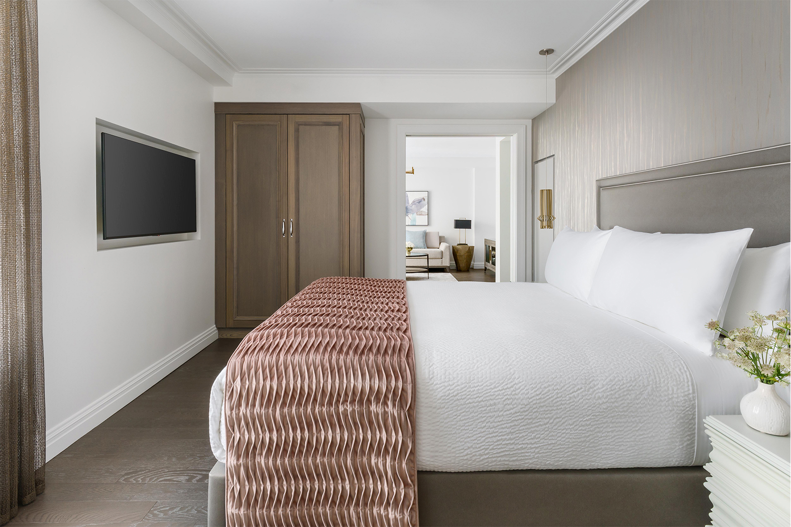 A wide view of a hotel room with a large bed, TV, wardrobe, and doorway to another room.